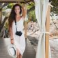 young natural beautiful woman in pale gown posing in marquee, tropical vacation, straw hat, digital photo camera, sensual, summer outfit, resort, boho vintage style, nature on background